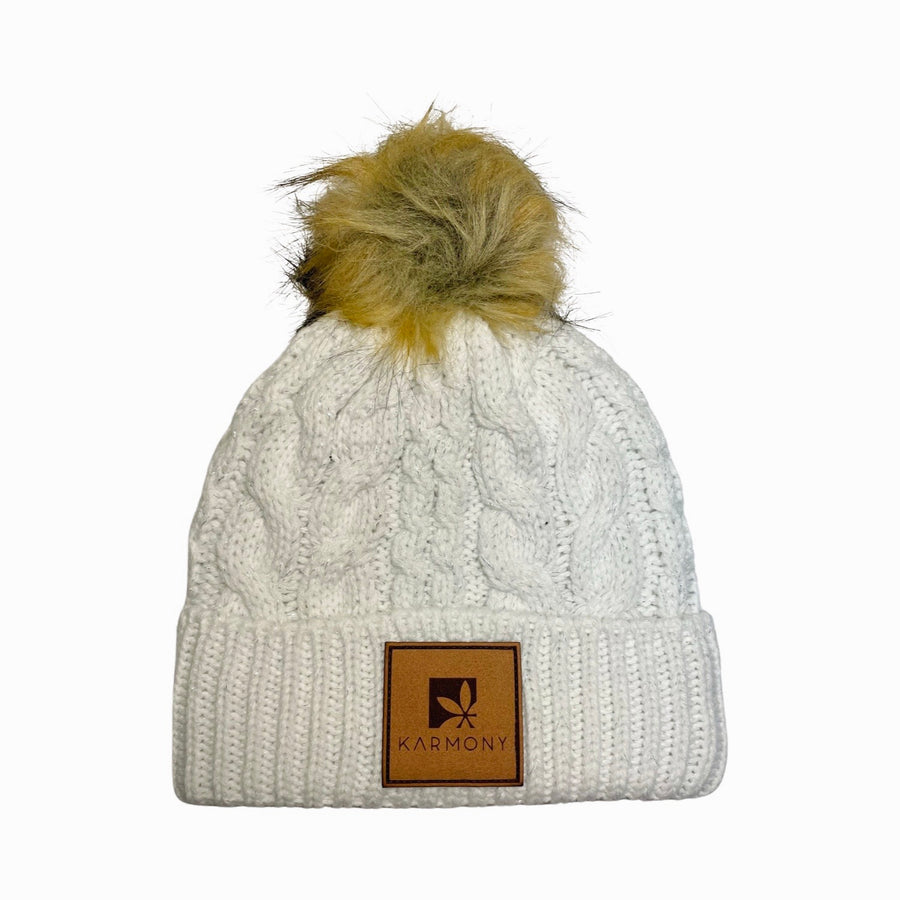 Cream beanie with silver metallic flecks and brown faux fur pompom. The brim has a leather patch of the Karmony logo.