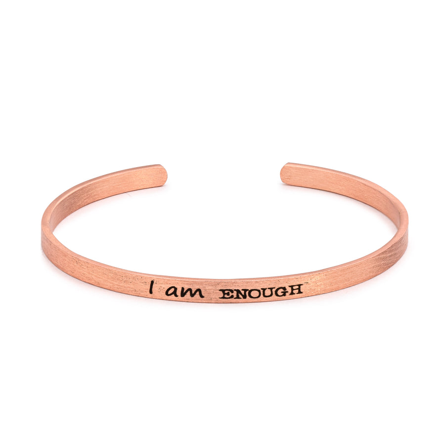 A slim brass cuff bracelet imprinted with black lettering.