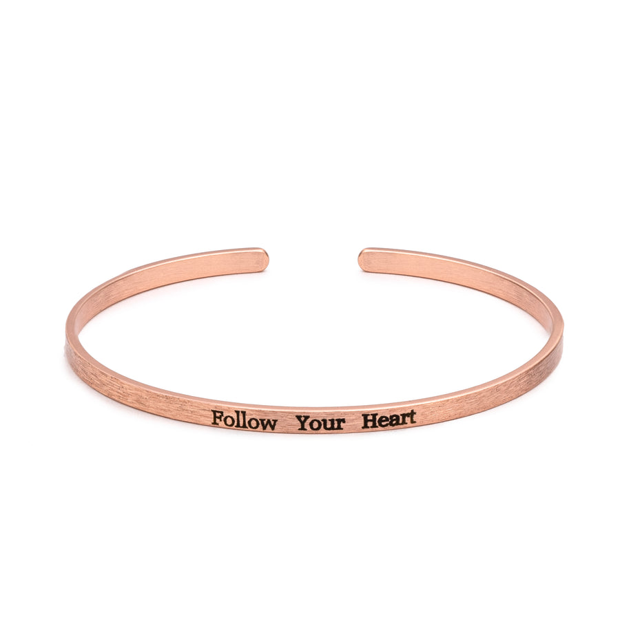 A slim brass cuff bracelet imprinted with black lettering.