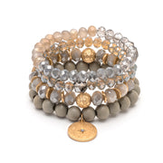 A bracelet of four stacked bands of beads, from off-white to grey. The bottom band has a round gold charm.