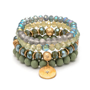 A bracelet of four stacked bands of beads, from light green to sage. The bottom band has a round gold charm.
