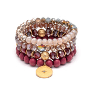A bracelet of four stacked bands of beads, from light pink to dark wine. The bottom band has a round gold charm.