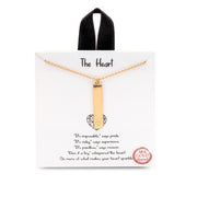 A gold charm necklace. The charm is a vertical bar with a small heart etched on the bottom.
