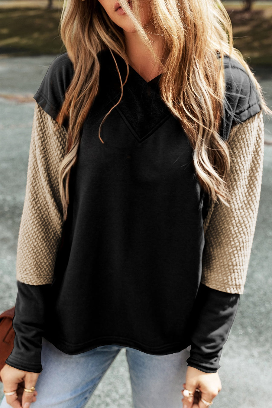 A black hooded sweatshirt with segmented sleeves. The largest middle segment is of textured tan fabric.