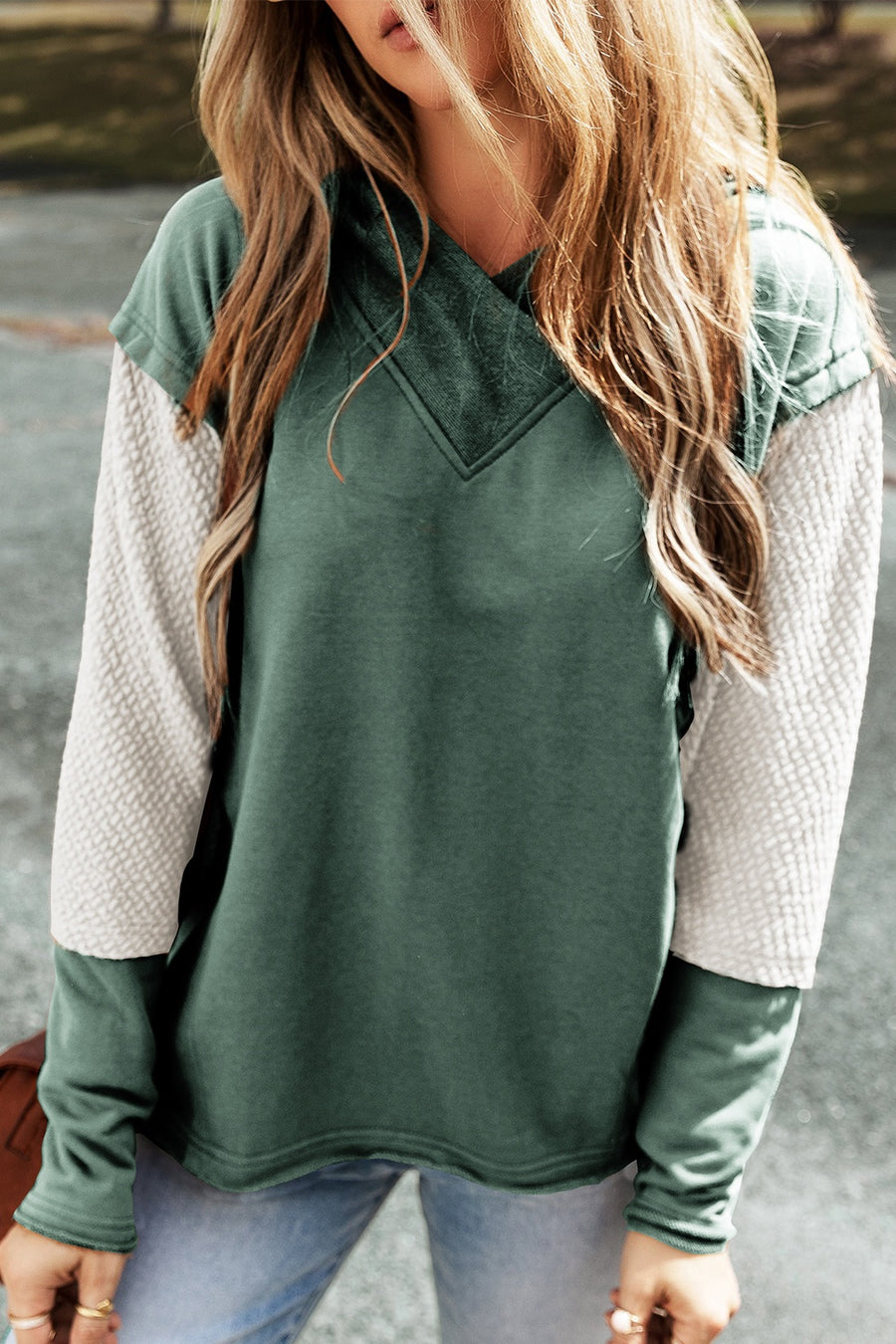 A sage green hooded sweatshirt with segmented sleeves. The largest middle segment is of textured white fabric.