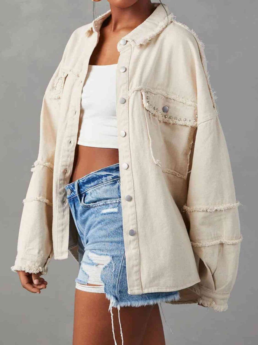 An off-white button-down denim jacket with raw hems on the collar, sleeves, and breast pockets. The pockets have silver studs along the flap. The buttons are flat silver.