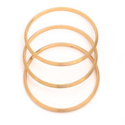 Satin Set of three Bangle Bracelets in matte gold layered and spaced over one another on white background