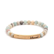 A bracelet of mixed turquoise, white, and grey stone beads, with a gold rectangular bar that reads "blessed".