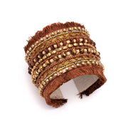 A thick cuff bracelet with brown beaded designs and fringe.