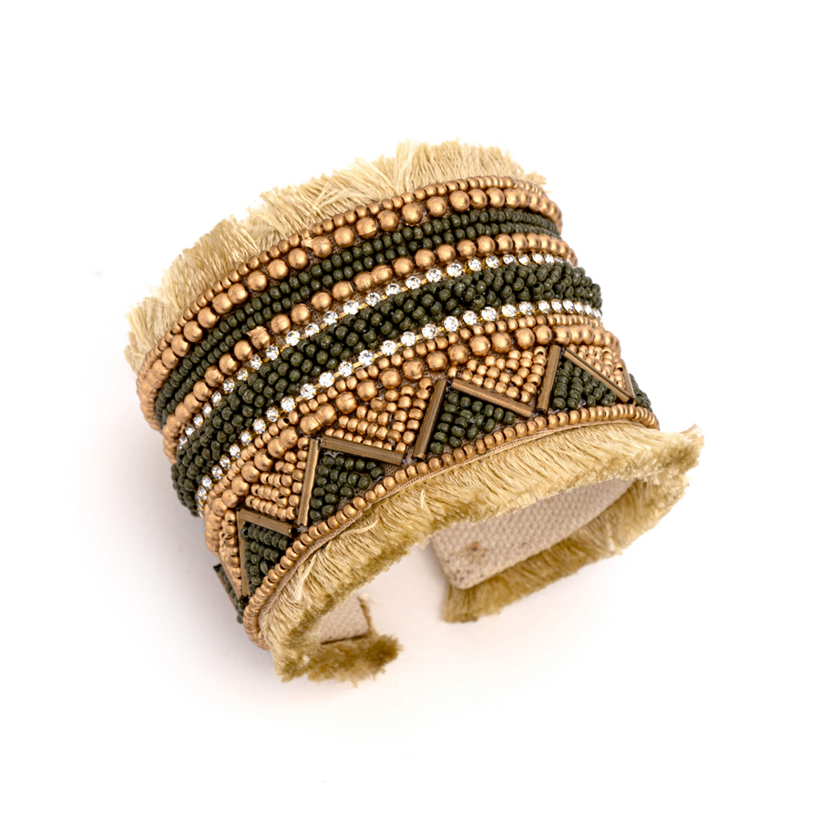 A thick cuff bracelet with tan and olive beaded designs and cream fringe.