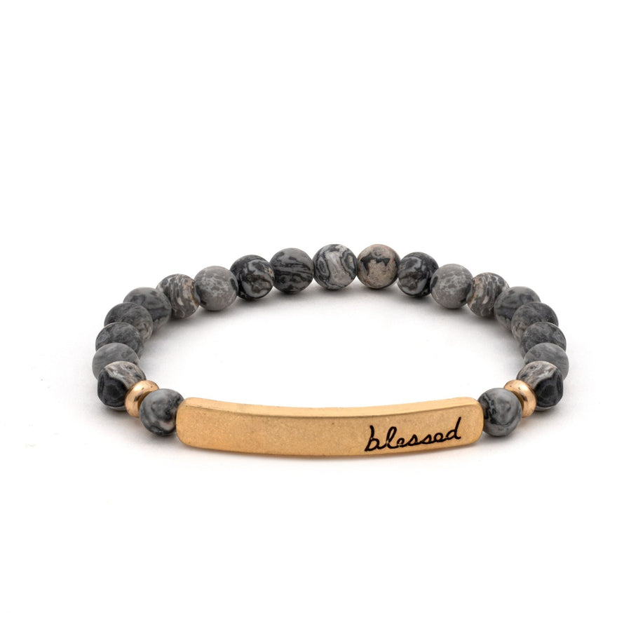 A bracelet of marbled grey and black stone beads, with a gold rectangular bar that reads "blessed".