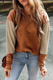 A caramel hooded sweatshirt with segmented sleeves. The largest middle segment is of textured tan fabric.