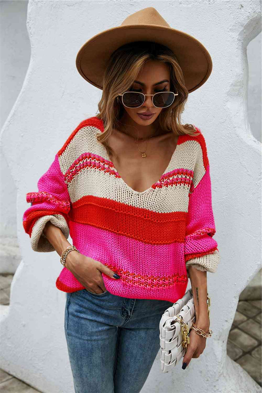 A baggy knit sweater of red, hot pink, and off-white horizontal stripes. The stripes are of varying widths.