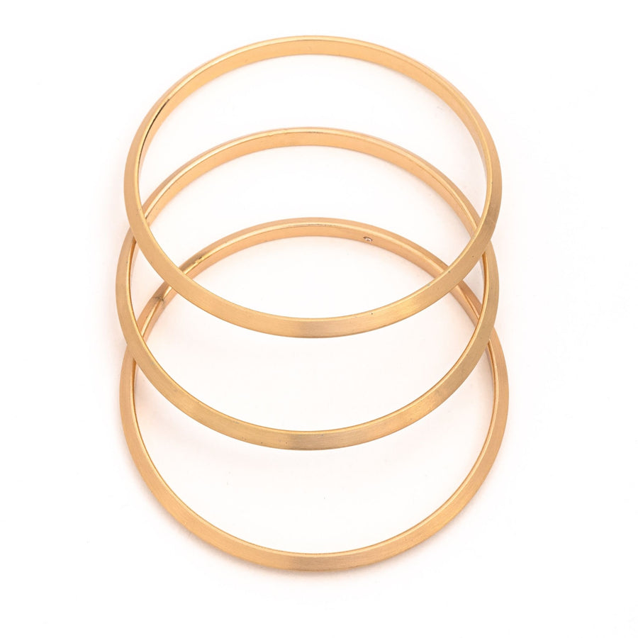 Satin Set of three Bangle Bracelets in matte gold layered and spaced over one another on white background
