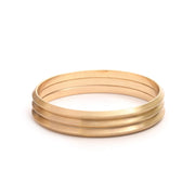 Satin Set of three Bangle Bracelets in matte gold stack on one another on white background